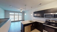 This single-floor residence in Wyoming, Michigan offers a thoughtfully designed open-concept layout that seamlessly connects the kitchen and living areas. The kitchen serves as a functional centerpiece, featuring dark espresso cabinetry with sleek hardware, granite countertops, and a full suite of stainless steel appliances including a refrigerator, range, microwave, and dishwasher. A peninsula with an integrated sink provides additional workspace and a natural division between the kitchen and living space. Pendant lighting above the peninsula and track lighting throughout the kitchen enhance the modern aesthetic.

The living area benefits from a large bank of windows that invites abundant natural light, offering views of the surrounding neighborhood. A ceiling fan adds practical comfort to the space. Light-toned wood-style flooring runs consistently throughout the main living areas, contributing to a clean, cohesive look.

The bathroom is well-equipped with a full tub and shower combination, a dark-cabineted vanity topped with granite, a large mirror, and textured neutral walls. Chrome fixtures and light wood-style flooring carry the modern finishes found throughout the rest of the unit, creating a consistent and polished overall ambiance.