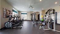 Located at 2845 Austin Manor Boulevard in Columbus, Ohio, this well-equipped fitness center offers a comprehensive workout environment spread across a single floor. The space is designed to accommodate a wide range of exercise needs, from cardiovascular training to strength conditioning.

The cardio area is home to multiple treadmills and elliptical machines, each equipped with individual screens for an engaging workout experience. Wall-mounted televisions and large mirrors line this section, enhancing the sense of space and allowing users to monitor their form. Natural light streams in through multiple windows fitted with blinds, keeping the environment bright and inviting.

The strength training area features a cable machine and a variety of resistance equipment, along with free weights and stability balls for functional fitness exercises. The dark rubber flooring throughout provides excellent traction and cushioning, ensuring both safety and comfort during workouts.

Recessed lighting and a ceiling fan contribute to a well-lit, ventilated atmosphere. The neutral-toned walls and clean layout give the space a professional yet approachable feel. Motivational fitness artwork adds personality to the walls, while large mirrors reflect light and help users maintain proper form. Glass-panel doors connect sections of the facility, maintaining an open and accessible flow throughout the space.