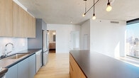 Located in Chicago's vibrant West Loop neighborhood, this contemporary single-floor residence at 234 W Polk St showcases a refined modern aesthetic throughout. Exposed concrete ceilings contrast beautifully with crisp white walls and light-toned hardwood flooring, creating a clean, industrial-chic atmosphere that runs consistently through every room.

The open living area is defined by dramatic floor-to-ceiling windows framed in sleek black, flooding the space with abundant natural light and offering sweeping views of the Chicago skyline. A wide-panel sliding glass door provides direct access to an outdoor balcony, further connecting the interior to the city beyond.

The kitchen is thoughtfully designed with two-tone cabinetry — light wood uppers paired with soft blue-gray lowers — complemented by dark quartz countertops, a marble-inspired tile backsplash, and a full suite of stainless steel Whirlpool appliances. A kitchen island with pendant lighting adds both function and style.

The bedrooms are bright and well-proportioned, with large windows and generous walk-in closet space. The primary bathroom features large-format dark tile flooring, a dual-sink vanity with light wood cabinetry, and a glass-enclosed walk-in shower with dark tile surround. A secondary bathroom echoes the same clean, contemporary finishes with a single-sink vanity and matching tile floors.