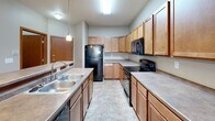 Located at 4877 28th Ave S in Fargo, North Dakota, this single-floor unit offers a functional and well-organized layout suited for comfortable everyday living. The kitchen is generously sized, featuring warm honey-toned wood cabinetry extending to the ceiling, ample counter space, tile flooring, and black appliances including a refrigerator, range, and built-in microwave, along with a double-basin sink. It connects seamlessly to the dining and living area, which is finished with plush carpet, a chandelier overhead, and a wall-mounted air conditioning unit complemented by baseboard heating. Multiple bedrooms are carpeted and bathed in natural light through sliding and double-pane windows that offer views of the surrounding neighborhood and greenery. Each room is serviced by baseboard heaters, ensuring year-round comfort. The bathrooms feature tile flooring, warm wood vanity cabinetry, and a full tub-shower combination. A dedicated in-unit laundry area houses a full-size washer and dryer with overhead wire shelving for added storage. Throughout the unit, warm beige and neutral tones create a cohesive, inviting atmosphere, while wood-trimmed doors and consistent finishes lend a sense of continuity across the space.