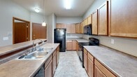 Located at 4877 28th Ave S in Fargo, North Dakota, this single-floor unit offers a functional and well-organized layout suited for comfortable everyday living. The kitchen is generously sized, featuring warm honey-toned wood cabinetry extending to the ceiling, ample counter space, tile flooring, and black appliances including a refrigerator, range, and built-in microwave, along with a double-basin sink. It connects seamlessly to the dining and living area, which is finished with plush carpet, a chandelier overhead, and a wall-mounted air conditioning unit complemented by baseboard heating. Multiple bedrooms are carpeted and bathed in natural light through sliding and double-pane windows that offer views of the surrounding neighborhood and greenery. Each room is serviced by baseboard heaters, ensuring year-round comfort. The bathrooms feature tile flooring, warm wood vanity cabinetry, and a full tub-shower combination. A dedicated in-unit laundry area houses a full-size washer and dryer with overhead wire shelving for added storage. Throughout the unit, warm beige and neutral tones create a cohesive, inviting atmosphere, while wood-trimmed doors and consistent finishes lend a sense of continuity across the space.