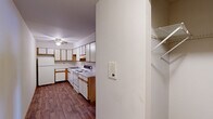 This single-floor space is designed with practicality and functionality in mind. The kitchen serves as a central feature, offering an efficient L-shaped layout with ample white cabinetry accented by warm wood-tone trim. White appliances, including a coil-burner electric range, dishwasher, and refrigerator, complement the clean white countertops. Wood-look flooring runs throughout the kitchen, adding warmth, while a ceiling fan provides air circulation overhead. A built-in intercom panel and adjacent closet with wire shelving are conveniently positioned near the kitchen entry.

The living and sleeping areas are finished with wall-to-wall carpet, creating a comfortable and quiet atmosphere. Ceiling fans are present in these rooms, and baseboard heating ensures year-round comfort. A window unit provides additional climate control in the bedroom, which also includes a closet accessible through a wood-trimmed door.

The bathroom is straightforward and clean, featuring a combined tub and shower enclosure, a toilet, and a vanity with storage beneath. Light tile flooring and a mirror with overhead lighting complete the space. Overall, the unit maintains a neutral, well-maintained palette throughout.
