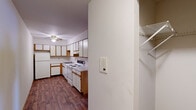 This single-floor space is designed with practicality and functionality in mind. The kitchen serves as a central feature, offering an efficient L-shaped layout with ample white cabinetry accented by warm wood-tone trim. White appliances, including a coil-burner electric range, dishwasher, and refrigerator, complement the clean white countertops. Wood-look flooring runs throughout the kitchen, adding warmth, while a ceiling fan provides air circulation overhead. A built-in intercom panel and adjacent closet with wire shelving are conveniently positioned near the kitchen entry.

The living and sleeping areas are finished with wall-to-wall carpet, creating a comfortable and quiet atmosphere. Ceiling fans are present in these rooms, and baseboard heating ensures year-round comfort. A window unit provides additional climate control in the bedroom, which also includes a closet accessible through a wood-trimmed door.

The bathroom is straightforward and clean, featuring a combined tub and shower enclosure, a toilet, and a vanity with storage beneath. Light tile flooring and a mirror with overhead lighting complete the space. Overall, the unit maintains a neutral, well-maintained palette throughout.