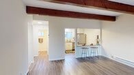 This two-floor space combines rustic charm with modern updates, creating a welcoming and functional environment. The living area is a standout, featuring dramatic exposed wood ceiling beams that add warmth and character to the otherwise clean, neutral palette. Hardwood-style flooring runs throughout the main living areas, complementing the bright, open feel of the space. A sliding glass door leads directly to a private outdoor patio, allowing natural light to pour in and providing easy access to the outdoors.

The kitchen is well-appointed with white shaker-style cabinetry, granite countertops, and stainless steel appliances, including a range and dishwasher. A pass-through breakfast bar with seating connects the kitchen to the living area, making it ideal for casual dining and entertaining. The upstairs level features carpeted bedrooms with mirrored closet doors and windows that bring in natural light and outdoor views.

Bathrooms are clean and updated, with one featuring a white vanity with a framed mirror and modern fixtures, and another offering a full tub and shower combination with hardwood-style flooring. Throughout the space, a consistent use of neutral tones, natural materials, and thoughtful updates creates a cohesive and comfortable atmosphere.