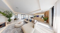 Located at 208 N Federal Hwy in Pompano Beach, Florida, this single-floor social club offers a generously sized, open-plan gathering space designed with a modern coastal aesthetic. The interior is defined by tray ceilings with integrated LED cove lighting that casts a warm, ambient glow throughout, complemented by large floor-to-ceiling sheer-draped windows that flood the space with natural light and offer views of the surrounding outdoors.

The main area is thoughtfully zoned into distinct social spaces. A central lounge features a large sectional sofa in cream leather, layered over a patterned area rug, with a sculptural round ottoman serving as a coffee table. Adjacent to this is a games zone anchored by a full-size black billiard table, flanked by modern bistro-height tables and wire-frame bar stools. A sleek bar counter with warm wood slat detailing serves as a focal point in the middle of the floor plan.

A dedicated media lounge tucked within the layout offers plush seating, a large wall-mounted television, and nautical-themed artwork, creating a more intimate retreat within the broader space. Throughout, lush tropical plants add vitality, while light-toned large-format tile flooring ties the entire space together. The overall ambiance is bright, sophisticated, and inviting—ideal for social gatherings and community events.