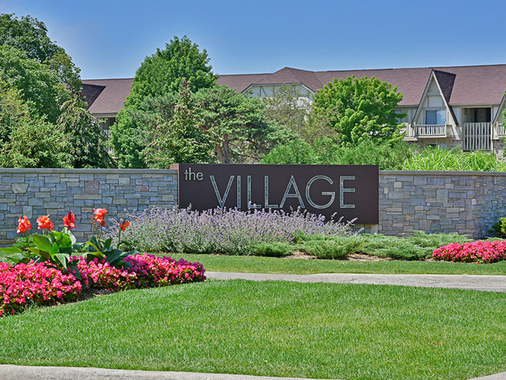 Letrero de entrada y jardín - The Village Apartments