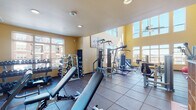 Located at 2674 N Park Ln in Fitchburg, Wisconsin, this two-floor fitness center offers a comprehensive and well-organized workout facility designed to accommodate a wide range of exercise needs. The main level features a spacious weight room with soaring double-height ceilings and an abundance of natural light streaming in through large upper clerestory windows and ground-level windows. This area is outfitted with a full complement of strength training equipment, including cable machines, multi-station weight systems, adjustable benches, and an extensive dumbbell rack. Rubber flooring throughout the weight room provides both safety and durability. A dedicated cardio zone houses multiple treadmills, stationary bikes, and additional cardio machines, all positioned near windows with exterior views. A separate cycling studio features spin bikes, hardwood flooring, and motivational artwork, creating an energetic atmosphere for group or individual cycling sessions. A staircase with a wood-and-glass railing leads to the second floor, which hosts a bright functional training room finished with hardwood floors. This space is equipped with stability balls, resistance bands, a wall-mounted mirror, and a mounted display screen, making it ideal for yoga, stretching, or personal training. A water fountain station is also conveniently available on the lower level.