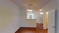 This two-story space in Denton, Texas offers a well-designed layout with classic architectural details throughout. The main living area features rich hardwood flooring that extends seamlessly toward the entryway, creating a warm and cohesive feel. Crown molding frames the ceilings, adding a refined touch to the interior.

A peninsula-style pass-through counter connects the kitchen to the living area, promoting an open flow between spaces. The kitchen receives natural light from a window overlooking the exterior, brightening the area during daytime hours. A pendant light with a classic glass shade hangs above, providing focused illumination and a decorative accent.

The entryway is defined by a solid paneled front door flanked by a transom window, allowing additional natural light into the foyer. A secondary interior door nearby suggests access to additional rooms or a closet. The neutral wall tones throughout complement the flooring and trim, creating a clean, versatile backdrop. The combination of traditional detailing and practical layout makes this space functional and inviting across both floors.