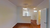 This two-story space in Denton, Texas offers a well-designed layout with classic architectural details throughout. The main living area features rich hardwood flooring that extends seamlessly toward the entryway, creating a warm and cohesive feel. Crown molding frames the ceilings, adding a refined touch to the interior.

A peninsula-style pass-through counter connects the kitchen to the living area, promoting an open flow between spaces. The kitchen receives natural light from a window overlooking the exterior, brightening the area during daytime hours. A pendant light with a classic glass shade hangs above, providing focused illumination and a decorative accent.

The entryway is defined by a solid paneled front door flanked by a transom window, allowing additional natural light into the foyer. A secondary interior door nearby suggests access to additional rooms or a closet. The neutral wall tones throughout complement the flooring and trim, creating a clean, versatile backdrop. The combination of traditional detailing and practical layout makes this space functional and inviting across both floors.