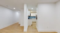This single-floor unit at Corner Grove Apartments, located at 601 West Cliveden Street in Philadelphia, PA, presents a clean, modern aesthetic achieved through a comprehensive renovation. Light wood-tone luxury flooring extends consistently throughout the entire space, complementing crisp white walls and bold white baseboards to create a bright, cohesive interior.

The open living area benefits from recessed lighting and a window that invites natural light, with a radiator positioned beneath it. Structural columns define the transition between the living space and the kitchen without fully enclosing either area, maintaining an open feel. The kitchen is a standout feature, showcasing white shaker-style cabinetry with matte black hardware, white quartz countertops, stainless steel appliances including a gas range and refrigerator, and a striking blue herringbone tile backsplash that adds a stylish focal point.

Two bathrooms serve the unit, each finished with geometric patterned tile in soft blue-gray tones and matte black fixtures. One bathroom includes a soaking tub, while the other features a walk-in shower with slate-toned floor tile. The bedrooms are generously proportioned, well-lit, and offer a neutral, move-in-ready canvas. In-unit laundry is also present, adding everyday convenience.