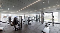 Located at 315 First Ave NE in Minneapolis, MN, this well-appointed fitness center offers a spacious, single-floor layout designed to accommodate a full range of workout activities. The facility features a thoughtfully organized arrangement of professional-grade equipment, including strength-training machines, cable systems, free weights, ellipticals, stationary bikes, and treadmills, providing users with a comprehensive exercise experience.

The interior design is contemporary and polished, with a paneled ceiling accented by linear LED lighting strips that cast a clean, even illumination throughout the space. The durable rubber flooring provides both safety and functionality, ideal for high-traffic fitness use. Structural concrete columns are integrated seamlessly into the design, adding an industrial aesthetic that complements the modern finishes.

Floor-to-ceiling windows line multiple walls, flooding the space with natural light and offering open views of the surrounding Minneapolis landscape, creating an energizing atmosphere for workouts. A large-format display screen is mounted on one wall, adding a multimedia element to the environment. The overall ambiance is bright, clean, and professional, making this fitness center a well-equipped destination for residents or users seeking a complete training facility.