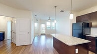 This single-floor residence offers a thoughtfully designed open-concept layout that seamlessly connects the kitchen and living area, creating a bright and functional living environment. The kitchen is a standout feature, showcasing rich dark-walnut cabinetry, granite countertops, a subway tile backsplash, and a large central island with pendant lighting overhead. Black appliances, including a refrigerator, range, microwave, and dishwasher, complement the cabinetry for a cohesive look. Wood-style flooring runs throughout the main living areas, reflecting abundant natural light that pours in through multiple windows. The living area is airy and open, enhanced by a ceiling fan and views to a private outdoor space through glass doors. The bedrooms offer a calm retreat, finished with plush wall-to-wall carpeting and natural light from windows with views of lush greenery. The bathroom is well-appointed with wood-style tile flooring, a granite-topped vanity with dark cabinetry, and a full tub-shower combination with floor-to-ceiling tile surround. Clean white walls and neutral tones throughout the space create a welcoming and versatile atmosphere suitable for a variety of lifestyle needs.