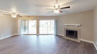 This single-floor unit offers a well-organized layout with consistent design elements throughout. The living area serves as a central highlight, featuring dark hardwood-style flooring, a ceiling fan with integrated lighting, and a textured ceiling. Large sliding glass doors span much of the wall, opening to an enclosed patio that brings in generous natural light and outdoor views. A tile-surround fireplace with a clean white mantel anchors one side of the living room, adding a functional and visual focal point.

The kitchen is outfitted with rich, dark cabinetry, granite-style countertops, a mosaic tile backsplash, and black appliances including a range, microwave, and refrigerator. Neutral-toned walls carry throughout each room, complementing the warm flooring.

The bedrooms feature ceiling fans, closets with built-in shelving and rods, and windows that bring in natural light. Each bedroom continues the dark hardwood-style flooring and maintains a clean, understated aesthetic.

Two bathrooms serve the unit. One features a walk-in shower with vertically stacked white tile, while the second includes a tub-shower combination with matching white tile surround. Both bathrooms include textured ceilings consistent with the rest of the unit.
