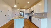 Located at 30 Main in Londonderry, NH, this thoughtfully designed single-floor residence combines modern finishes with functional living spaces. The kitchen serves as the heart of the home, showcasing crisp white shaker cabinetry, a subway tile backsplash, and a spacious center island topped with striking granite countertops. Pendant lighting illuminates the island, which features an undermount sink, while stainless steel appliances — including a French door refrigerator with ice maker, over-the-range microwave, and a gas range — complete the chef-ready setup. Rich hardwood flooring extends throughout the main living areas, adding warmth and continuity to the open layout. The living area is generously proportioned, with neutral walls and recessed lighting that create a bright, welcoming atmosphere. The bedroom is carpeted for comfort and features dual windows that bring in natural light and offer outdoor views. The bathroom is clean and contemporary, appointed with a soaking tub and shower combo, a grey shaker-style vanity with white countertop, a framed mirror, and a tall linen cabinet for added storage. Light tile flooring ties the space together. A dedicated laundry closet houses a full-size washer and dryer with overhead shelving, providing excellent in-unit convenience.