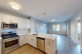 This thoughtfully designed one-bedroom, one-bathroom residence in Fall River, Massachusetts offers a functional and modern single-floor layout. The open-concept kitchen flows seamlessly into the combined dining and living area, creating an inviting and spacious atmosphere. The kitchen is equipped with stainless steel appliances—including a gas range, microwave, refrigerator with ice maker, and dishwasher—complemented by crisp white shaker cabinetry, white quartz countertops, a peninsula with pendant lighting, and a stainless steel sink. Warm hardwood-style flooring runs throughout the main living areas, adding a cohesive and contemporary feel. The bedroom features plush carpeting, neutral-toned walls, and a window that brings in natural light. The full bathroom is finished with light tile flooring, a white vanity with quartz countertop, a wall-mounted mirror, and a shower/tub combination. Additional highlights include three closets for ample storage, a dedicated laundry area, a utility room, and a private patio overlooking landscaped grounds. The entrance features a bold dark-paneled front door, setting a polished tone upon arrival. This residence combines practical amenities with clean, modern design throughout.