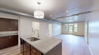 This well-appointed three-bedroom, two-bathroom unit at 230 E 30th Street in Kansas City, Missouri offers a thoughtfully designed single-level floor plan with a cohesive blend of modern finishes throughout. The open-concept kitchen serves as the centerpiece, featuring rich dark-stained cabinetry, granite countertops, a large island with an integrated sink, pendant lighting, and light hardwood-style flooring — ideal for both cooking and entertaining. Exposed ductwork along the ceiling adds an industrial character to the living area, which opens to a balcony through French doors, filling the space with natural light and urban views. Each of the three bedrooms is carpeted and equipped with ceiling fans, with windows offering city views. The spacious primary bedroom provides a comfortable retreat. The two bathrooms are finished with marble-style tile surrounds, dark vanity cabinetry, and granite countertops — one featuring a glass-enclosed walk-in shower, the other a full soaking tub. A dedicated laundry room houses a full-size washer and dryer with overhead shelving for added storage. A closet and multiple hallways contribute to practical circulation throughout the unit.