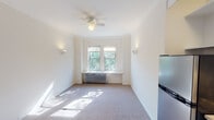 Located at 5747 N Winthrop Ave in Chicago's Edgewater neighborhood, this single-floor studio unit offers a functional and well-organized layout. The main living area is bright and open, featuring soft carpeting, crown molding, and a ceiling fan with light fixture. Wall sconces provide warm ambient lighting, while a pair of double-hung windows frame views of surrounding greenery, allowing natural light to fill the space. A classic cast-iron radiator beneath the windows provides efficient heating. The compact kitchen is efficiently designed with white cabinetry, white subway tile backsplash, a stainless steel refrigerator, a gas range, and a single-basin stainless steel sink — offering all essential appliances in a tidy, organized footprint. The bathroom carries a clean, classic aesthetic with white penny-tile flooring, full subway tile wall surround, a pedestal-style vanity, mirrored medicine cabinet with open shelving, and a shower-tub combination with dual windows for natural ventilation. The overall ambiance of the unit is clean and functional, with traditional architectural details such as crown molding lending character throughout. The space is well-suited for those seeking a practical urban residence in a vibrant Chicago neighborhood.
