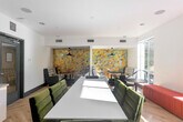 Located at 500 Race St in San Jose, California, this thoughtfully designed communal lounge space offers a compelling blend of modern aesthetics and functional versatility. The single-floor layout is unified by light-toned herringbone hardwood flooring that adds warmth and visual interest throughout.

Natural light pours in through large, floor-to-ceiling windows lining multiple walls, offering views of the surrounding streetscape and mature trees. Recessed ceiling lighting complements the abundant daylight, ensuring the space remains bright at all times.

Seating is diverse and carefully curated: plaid-upholstered sofas and gray armchairs form intimate conversation nooks, while a bold terracotta-red banquette runs along one windowed wall, paired with round café-style tables. A central white conference table with velvet green chairs provides a dedicated workspace or meeting area.

A striking multi-toned hexagonal tile feature wall in warm earth tones serves as a bold focal point, anchored by sleek pendant lights. On the opposite end, a large abstract geological artwork hangs above a built-in white cabinetry unit with a gray countertop and open shelving—ideal for storage or display.

The space is completed by a glazed entry door, ceiling-mounted speakers, and HVAC vents, reflecting a polished, amenity-rich environment suited for collaboration, socializing, or focused work.