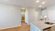 This single-floor residence in Huntsville, Alabama offers a thoughtfully designed layout with a clean, contemporary aesthetic throughout. Soft sage-toned walls, white trim, and recessed lighting create a bright, cohesive atmosphere across all rooms.

The open-concept kitchen serves as a central highlight, featuring white shaker-style cabinetry, granite countertops, and a peninsula island with an undermount sink. Stainless steel appliances, including a range, microwave, and refrigerator, complement the modern finishes. Warm hardwood-style flooring extends throughout the main living areas, enhancing the sense of openness.

The living area benefits from natural light through large windows and a glass-paneled door that leads to a private balcony, offering views of the surrounding community. A ceiling fan adds comfort to both the living room and bedroom spaces.

The bedrooms are finished with plush carpeting and include access to closet space. The primary bedroom connects directly to a bathroom featuring a soaking tub with a tiled shower surround, vanity with warm-toned cabinetry, and an adjacent walk-in closet with built-in shelving. The overall design balances practicality with polished, move-in-ready finishes.