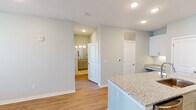 This single-floor residence in Huntsville, Alabama offers a thoughtfully designed layout with a clean, contemporary aesthetic throughout. Soft sage-toned walls, white trim, and recessed lighting create a bright, cohesive atmosphere across all rooms.

The open-concept kitchen serves as a central highlight, featuring white shaker-style cabinetry, granite countertops, and a peninsula island with an undermount sink. Stainless steel appliances, including a range, microwave, and refrigerator, complement the modern finishes. Warm hardwood-style flooring extends throughout the main living areas, enhancing the sense of openness.

The living area benefits from natural light through large windows and a glass-paneled door that leads to a private balcony, offering views of the surrounding community. A ceiling fan adds comfort to both the living room and bedroom spaces.

The bedrooms are finished with plush carpeting and include access to closet space. The primary bedroom connects directly to a bathroom featuring a soaking tub with a tiled shower surround, vanity with warm-toned cabinetry, and an adjacent walk-in closet with built-in shelving. The overall design balances practicality with polished, move-in-ready finishes.