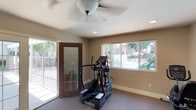 The fitness center at 854 Vine St in Oceanside is a single-story facility designed to provide residents with a functional and comfortable workout environment. The space is organized across several connected areas, each housing a variety of exercise equipment. Cardio options include an elliptical trainer and a stationary recumbent bike, while a multi-station strength training machine with a rowing attachment serves those seeking resistance workouts. Additional free weights and accessories are also available throughout the space.

Natural light is a defining feature of the main workout area, where large windows and glass-paneled doors open toward an outdoor pool and landscaped courtyard, providing pleasant views and a bright, airy atmosphere. Ceiling fans are installed throughout to maintain comfortable airflow during workouts. The floors are covered in low-pile carpet suited for fitness use, and recessed lighting supplements natural light in the interior sections.

Practical amenities include wall-mounted paper towel and hand sanitizer dispensers, posted exercise room rules, and a no-smoking policy, reflecting an emphasis on cleanliness and courtesy. The space offers a well-rounded, accessible fitness option within a community setting.