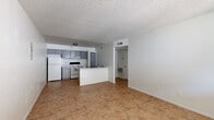 Located at 6801 N 25th Dr in Phoenix, AZ, this single-story, one-bedroom, one-bathroom unit offers a practical and well-organized layout. The open-concept living and kitchen area forms the heart of the space, featuring warm terra-cotta-toned tile flooring, a textured ceiling, and a peninsula counter that separates the kitchen from the living area. The kitchen is equipped with gray cabinetry, white appliances including a refrigerator and electric range, an under-cabinet range hood, and a single-basin sink on the peninsula. The living area is bright and airy, with a window allowing natural light to filter in and a front entry door providing direct access. A hallway connects the main living space to the private areas of the unit. The bedroom is a comfortable size, featuring warm carpeting, a window for natural light, and access to a dedicated walk-in closet complete with a hanging rod for storage. The full bathroom includes a shower-tub combination, toilet, and a vanity with sink. Throughout the unit, the clean white walls and consistent finishes create a cohesive, straightforward living environment well-suited for single occupancy.