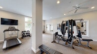 Located at 800 Ellington Cir in Gahanna, Ohio, this community fitness center offers a well-equipped, single-floor workout facility designed to support a comprehensive exercise routine. The space is finished with neutral-toned walls and plush carpet flooring, creating a clean and comfortable environment for residents.

The facility is generously lit by abundant natural light streaming through multiple large windows with horizontal blinds, complemented by recessed ceiling lighting and a ceiling fan that helps maintain a comfortable atmosphere during workouts. Structural columns punctuate the open floor plan, adding architectural character without disrupting the flow of the space.

Cardio equipment includes treadmills, a stationary upright bike, a spin bike, and a stair-step machine, all positioned near the windows to take advantage of the outdoor views. A wall-mounted flat-screen television provides entertainment during cardio sessions. The strength training area features a multi-station cable machine, a weight bench, and a well-stocked dumbbell rack. Large framed wall mirrors throughout the space enhance the sense of openness and allow users to monitor their form.

A dedicated entry area includes a side table stocked with sanitizing wipes and a waste bin, emphasizing cleanliness and convenience. Additional amenities include wall art, a coat rack, and keypad-secured access. The fitness center also connects to adjacent community spaces, including a theater room visible through the interior windows.