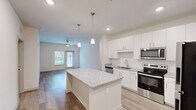 Located at 125 New Hanover St in Beaufort, SC, this well-appointed single-story home offers three bedrooms and two bathrooms with a clean, modern aesthetic throughout. The open-concept kitchen and living area serves as the heart of the home, anchored by a large granite-topped center island with pendant lighting overhead. White shaker cabinetry, a stainless steel appliance suite including a range, microwave, dishwasher, and refrigerator, and a undermount sink complete the kitchen. The living area extends naturally from the kitchen, featuring wood-look flooring, a ceiling fan, and a glass door that brings in natural light. Each bedroom is bright and inviting, outfitted with ceiling fans, wood-look flooring, and windows with blinds. The spacious primary bedroom includes access to a generous walk-in closet with extensive wire shelving for ample storage. The bathrooms mirror the home's refined finishes, showcasing granite vanity countertops, white cabinetry, large mirrors, and tile-surround walk-in showers. A dedicated utility room adds everyday convenience. Neutral tones, recessed lighting, and consistent flooring throughout lend the home a cohesive and contemporary feel.
