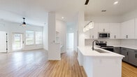 This single-story home showcases a clean, modern design with consistent warm-toned hardwood-style flooring and crisp white walls throughout. The open-concept layout connects the living area and kitchen seamlessly, creating a spacious, airy feel enhanced by recessed lighting and natural light from multiple windows.

The kitchen is a standout feature, equipped with stainless steel appliances including a French door refrigerator, electric range, and microwave. Two-toned cabinetry pairs white upper cabinets with gray lower cabinets, accented by a classic subway tile backsplash and white countertops. A peninsula with an undermount sink and pendant lighting above adds both functionality and style.

The living area is generously sized with a ceiling fan and front-facing windows that invite natural light. A built-in shelving nook adds a practical architectural detail. The bedrooms are well-proportioned, each featuring ample closet space and continued hardwood-style flooring.

Two bathrooms serve the home: one featuring a glass-enclosed walk-in shower with black hardware accents and a gray vanity, and a second with a tub-shower combination, matching gray cabinetry, and coordinating black fixtures. The cohesive design palette and modern finishes give the entire space a fresh, move-in-ready appeal.