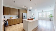 This thoughtfully designed single-floor residence combines modern aesthetics with functional living. The heart of the home is an open-concept kitchen that flows seamlessly into the living area. The kitchen is outfitted with flat-front wood-tone cabinetry extending to the ceiling, crisp white quartz countertops, a full suite of stainless steel appliances including a French door refrigerator, electric range, and built-in microwave. A generously sized center island with an undermount sink and pendant lighting above serves as both a prep space and gathering point. Track lighting and light wood-tone flooring complete the kitchen's contemporary feel. The adjoining living area is bright and open, benefiting from natural light through large windows and a ceiling fan overhead. The bedrooms feature plush carpeting, ceiling fans, and large windows that invite natural light and outdoor views. The primary bathroom offers a spacious layout with dark wood-tone cabinetry, a white quartz vanity, a glass-enclosed shower, and large-format tile flooring. A secondary bathroom provides a full tub-shower combination with tiled surround and dark cabinetry for storage. Throughout the residence, clean white walls, consistent finishes, and a neutral palette create a cohesive and inviting atmosphere.