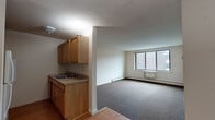 Located at 1021 Asylum Ave in Hartford, Connecticut, this single-floor residential unit offers a practical and functional layout. The open-concept living and dining area is generously sized, featuring neutral-toned carpet flooring and a large window that allows natural light to fill the space while providing views of the surrounding urban neighborhood. A baseboard heating system runs along the perimeter, ensuring year-round comfort.

The kitchen is efficiently designed with warm wood cabinetry, a granite-look countertop, a single-basin sink, and a white range stove. The kitchen transitions seamlessly into the living area, with hardwood flooring underfoot that adds warmth and contrast to the carpeted living space. A dedicated entry area near the front door provides a clear transition point into the unit.

The bedroom is a well-proportioned room with carpet flooring, neutral walls, and a window overlooking the adjacent building, allowing for natural light and ventilation. Baseboard heating is also present in this room.

The bathroom is neatly appointed with a wood-vanity cabinet, a single-basin sink with a mirrored medicine cabinet above, tile-surround walls, and a shower-tub combination enclosed by a gold-framed sliding glass door. The overall unit presents a clean, straightforward layout suitable for everyday living.