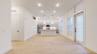 This single-floor residence showcases a clean, contemporary design with a bright, open-concept layout. Light hardwood flooring flows seamlessly throughout the main living areas, complementing the crisp white walls and abundant recessed lighting. The kitchen serves as the heart of the home, anchored by a large white center island with pendant lighting above and dark hardware accents. Light wood cabinetry extends to the ceiling, providing generous storage, while stainless steel appliances — including a gas range, built-in microwave, and French door refrigerator — add a polished, functional touch. A vertical tile backsplash and quartz countertops complete the modern aesthetic. Tall windows along one wall flood the space with natural light. The bedrooms feature the same light hardwood flooring, ceiling fans, and built-in closet systems, including a spacious walk-in closet with multi-level shelving and hanging rods. The bathrooms are finished with large-format marble-look tile, gray vanity cabinets, white quartz countertops, black hardware accents, and frameless glass shower enclosures. Throughout the residence, thoughtful architectural details — including crown molding, decorative wall niches, and a cohesive neutral palette — create a refined yet inviting atmosphere.