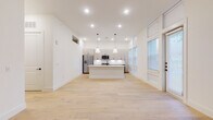 This single-floor residence showcases a clean, contemporary design with a bright, open-concept layout. Light hardwood flooring flows seamlessly throughout the main living areas, complementing the crisp white walls and abundant recessed lighting. The kitchen serves as the heart of the home, anchored by a large white center island with pendant lighting above and dark hardware accents. Light wood cabinetry extends to the ceiling, providing generous storage, while stainless steel appliances — including a gas range, built-in microwave, and French door refrigerator — add a polished, functional touch. A vertical tile backsplash and quartz countertops complete the modern aesthetic. Tall windows along one wall flood the space with natural light. The bedrooms feature the same light hardwood flooring, ceiling fans, and built-in closet systems, including a spacious walk-in closet with multi-level shelving and hanging rods. The bathrooms are finished with large-format marble-look tile, gray vanity cabinets, white quartz countertops, black hardware accents, and frameless glass shower enclosures. Throughout the residence, thoughtful architectural details — including crown molding, decorative wall niches, and a cohesive neutral palette — create a refined yet inviting atmosphere.