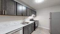 Located at 1699 Shanley Dr in Columbus, Ohio, this single-floor residence offers a practical and updated living environment with a clean, neutral aesthetic throughout. The open living area is finished with plush wall-to-wall carpeting and textured ceilings, providing a comfortable and versatile space that flows naturally into adjacent rooms. Neutral-toned walls and white baseboards contribute to a bright, cohesive atmosphere throughout.

The kitchen is a standout feature, showcasing dark charcoal shaker-style cabinetry paired with modern stainless steel hardware. Marble-look countertops add a refined touch, complemented by a stainless steel sink with a contemporary spring-neck faucet. Stainless steel appliances — including a gas range and dishwasher — complete the well-appointed kitchen, which features light wood-look flooring for easy maintenance.

The bedroom includes a built-in closet with a hanging rod and upper shelf, offering practical storage solutions, with soft carpeting underfoot. The bathroom is clean and functional, featuring a full tub-shower combination, a white vanity with cabinet storage, and light wood-look flooring. Overall, the space presents a well-maintained and updated interior suitable for comfortable everyday living.
