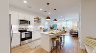 This thoughtfully designed two-bedroom, four-bathroom residence in Austin, TX delivers a clean, modern aesthetic across a well-organized single-floor layout. The open-concept kitchen serves as a central hub, featuring white shaker cabinetry, stainless steel appliances, subway tile backsplash, and a central island with bar seating illuminated by warm brass pendant lights. Light wood-look flooring flows seamlessly from the kitchen into the living area, which benefits from natural light through large windows dressed with sheer curtains and a ceiling fan overhead. Both bedrooms offer carpeted flooring, dedicated closet storage with built-in shelving, and windows that bring in natural light. The primary bedroom is a comfortable retreat with its own well-appointed closet. The bathrooms are finished in crisp white with wide vanities, large mirrors, and a tub-shower combination. A second living area provides flexible space for a home office or lounge. The overall ambiance is bright and cohesive, with neutral tones, recessed lighting, and consistent modern finishes creating a welcoming, functional living environment.
