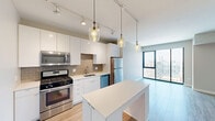 Located in Chicago's vibrant River North neighborhood, this modern one-bedroom, one-bathroom unit offers a well-designed layout with contemporary finishes throughout. Light wood-style flooring flows seamlessly across the entire space, creating a cohesive and airy feel.

The open-concept kitchen and living area serves as the heart of the unit. The kitchen is outfitted with sleek white cabinetry extending to the ceiling, a warm tan subway tile backsplash, stainless steel appliances including a gas range, microwave, dishwasher, and refrigerator, and a white waterfall-edge island that doubles as a dining and prep surface. Stylish glass pendant lights and a track lighting system illuminate the space with both ambient and task lighting.

The living area opens to large floor-to-ceiling windows that frame sweeping Chicago skyline views, filling the space with abundant natural light. The bedroom is a comfortable size, featuring two black-framed windows that continue the city views, and is complemented by a dedicated walk-in closet with built-in wire shelving and hanging rods for ample storage.

The bathroom is finished with large-format light tile flooring and clean, neutral walls, maintaining the modern aesthetic found throughout. This thoughtfully designed unit offers a streamlined urban living experience in one of Chicago's most sought-after neighborhoods.