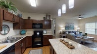 This single-floor residence offers a thoughtfully designed open-concept layout that seamlessly connects the kitchen, dining, and living areas. The kitchen is a standout feature, showcasing rich dark wood cabinetry, granite countertops, black appliances including a range, built-in microwave, dishwasher, and refrigerator, as well as a central island with bar seating beneath a trio of stylish pendant lights — ideal for casual dining or entertaining. Wood-style flooring runs throughout the main living areas, adding warmth and continuity to the space.

The living room is generously proportioned, filled with natural light from a large window, and features a ceiling fan overhead. The bedroom continues the warm, comfortable aesthetic with plush carpeting, a ceiling fan, and large windows that frame outdoor greenery, offering a peaceful retreat.

The bathroom is well-appointed with granite countertops, a wood-tone vanity, and a full tub-shower combination. A dedicated laundry room with a full-size washer and dryer adds everyday convenience. A built-in niche near the entryway provides a welcoming touch upon arrival. Throughout the residence, neutral tones and consistent finishes create a cohesive, move-in-ready atmosphere.