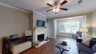 Located at 1128 Whisperwood Ct in Greensboro, NC, this single-floor residence offers a well-appointed layout designed for comfortable living. The spacious living room serves as the heart of the home, highlighted by a classic white-mantled fireplace, crown molding, a ceiling fan with lighting, and rich hardwood-style flooring. A large window at the far end of the room floods the space with natural light and provides views of the surrounding greenery, enhancing the open, airy feel.

The kitchen is efficiently designed with dark shaker-style cabinetry, granite countertops, and stainless steel appliances including a refrigerator and dishwasher. Hardwood-style flooring continues seamlessly into the adjacent dining area, which features crown molding and a wainscoting accent wall.

Two bedrooms offer carpeted floors, ceiling fans, and windows that bring in natural light. Both are well-sized and provide a calm, comfortable atmosphere. The two bathrooms are consistent in finish, each featuring dark vanity cabinetry with granite countertops, hardwood-style flooring, and tub-shower combinations with curved curtain rods, presenting a clean, cohesive aesthetic throughout.