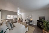 Located at 1501 Harvey Road in College Station, TX, this studio unit offers a thoughtfully designed single-floor layout that maximizes every square foot. The open-concept main area seamlessly combines the living, dining, and kitchen spaces into one cohesive room. Wood-look flooring runs throughout, lending a warm, contemporary feel, while a textured ceiling and ceiling fan add classic character overhead.

The living and sleeping area is generously proportioned for a studio, accommodating a full-sized bed alongside a dedicated workspace with a dark wood desk. Framed wall art and neutral gray tones create a calm, sophisticated atmosphere. A window with blinds and curtains allows natural light to filter into the space.

The kitchen is accessible via a pass-through counter with bar seating, offering a practical and social layout. White cabinetry and appliances keep the kitchen clean and functional.

Two bathrooms serve this unit — a notable feature for a studio — each finished with light gray cabinetry, a vanity with a large mirror, and bright overhead lighting. One bathroom includes a full tub-shower combination with tiled surround. A dedicated closet provides additional storage. The overall design is cohesive and move-in ready, making it a practical and comfortable option in the heart of College Station.