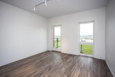 This single-floor unit offers a clean, modern aesthetic defined by neutral tones, warm hardwood-style flooring, and an efficient, well-organized layout. The main living area is bright and open, featuring elevated ceilings, track lighting, and two large windows — one of which leads to a private balcony — that flood the space with natural light and provide sweeping outdoor views of the surrounding greenery and neighboring structures. The airy, minimalist design of this room makes it highly versatile and easy to furnish. The bedroom is a comfortable, quiet space with recessed and track lighting, clean white walls, and the same hardwood-style flooring that runs throughout the unit, creating a cohesive look and feel. The kitchen is well-appointed with crisp white shaker-style cabinetry, light countertops, a stainless steel double-basin sink, and stainless steel appliances including an electric range and an over-the-range microwave — offering both functionality and a contemporary style. The bathroom maintains the unit's clean design with white fixtures, a full soaking tub, a towel bar, and hardwood-style flooring that ties the space together. Overall, this unit presents a bright, functional, and modern living environment.