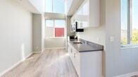 Located at 4229 7th Ave NE in Seattle's vibrant University District, this efficiently designed studio unit offers a thoughtfully organized single-floor layout. Light hardwood-style flooring runs throughout, complementing the clean, neutral palette of soft gray and white tones that give the space a bright, modern feel.

The kitchen is a standout feature, equipped with sleek white cabinetry — both upper and lower — topped with gray laminate countertops. A stainless steel sink, built-in cooktop, over-the-range microwave, and compact refrigerator provide all essential amenities. A large window positioned above the kitchen area allows natural light to pour in, enhancing the open feel of the space.

The living area is anchored by a generous window offering views of surrounding greenery, creating a connection to the outdoors. A built-in closet with open shelving provides practical storage within the compact footprint.

The bathroom features wood-style flooring, a white vanity with sink, a subway tile shower stall with grab bars, and open shelving for additional storage. Flush-mount ceiling lighting is present throughout, ensuring consistent illumination. The entry door leads into a clean hallway that connects all areas of the unit seamlessly, making this a functional and well-appointed space in a prime Seattle location.