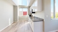 Located at 4229 7th Ave NE in Seattle's vibrant University District, this efficiently designed studio unit offers a thoughtfully organized single-floor layout. Light hardwood-style flooring runs throughout, complementing the clean, neutral palette of soft gray and white tones that give the space a bright, modern feel.

The kitchen is a standout feature, equipped with sleek white cabinetry — both upper and lower — topped with gray laminate countertops. A stainless steel sink, built-in cooktop, over-the-range microwave, and compact refrigerator provide all essential amenities. A large window positioned above the kitchen area allows natural light to pour in, enhancing the open feel of the space.

The living area is anchored by a generous window offering views of surrounding greenery, creating a connection to the outdoors. A built-in closet with open shelving provides practical storage within the compact footprint.

The bathroom features wood-style flooring, a white vanity with sink, a subway tile shower stall with grab bars, and open shelving for additional storage. Flush-mount ceiling lighting is present throughout, ensuring consistent illumination. The entry door leads into a clean hallway that connects all areas of the unit seamlessly, making this a functional and well-appointed space in a prime Seattle location.