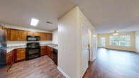 Located at 3011 Stone Carriage Cir in Fayetteville, NC, this single-floor home offers a well-designed layout with a range of functional features throughout. The kitchen is equipped with warm-toned wood cabinetry, granite-style countertops, and black appliances including an electric range, over-the-range microwave, and dishwasher. A skylight provides additional natural light to the cooking space, which flows conveniently into the main corridor. The open living area features durable wood-style flooring and a ceiling fan with integrated lighting, creating a bright and airy atmosphere. A windowed bedroom with plush carpeting and a ceiling fan offers a comfortable retreat, accompanied by a double-door closet with built-in shelving for ample storage. The primary bathroom includes a vanity with generous counter space, wood cabinetry, and direct access to a spacious walk-in closet outfitted with wire shelving. A full soaking tub with a shower surround completes the bathroom. An additional carpeted bedroom also features a double-door closet. The home includes a dedicated in-unit laundry area with a full-size washer and dryer. Warm cream-toned walls and consistent wood-style flooring unify the interior, contributing to a cohesive and practical living environment.