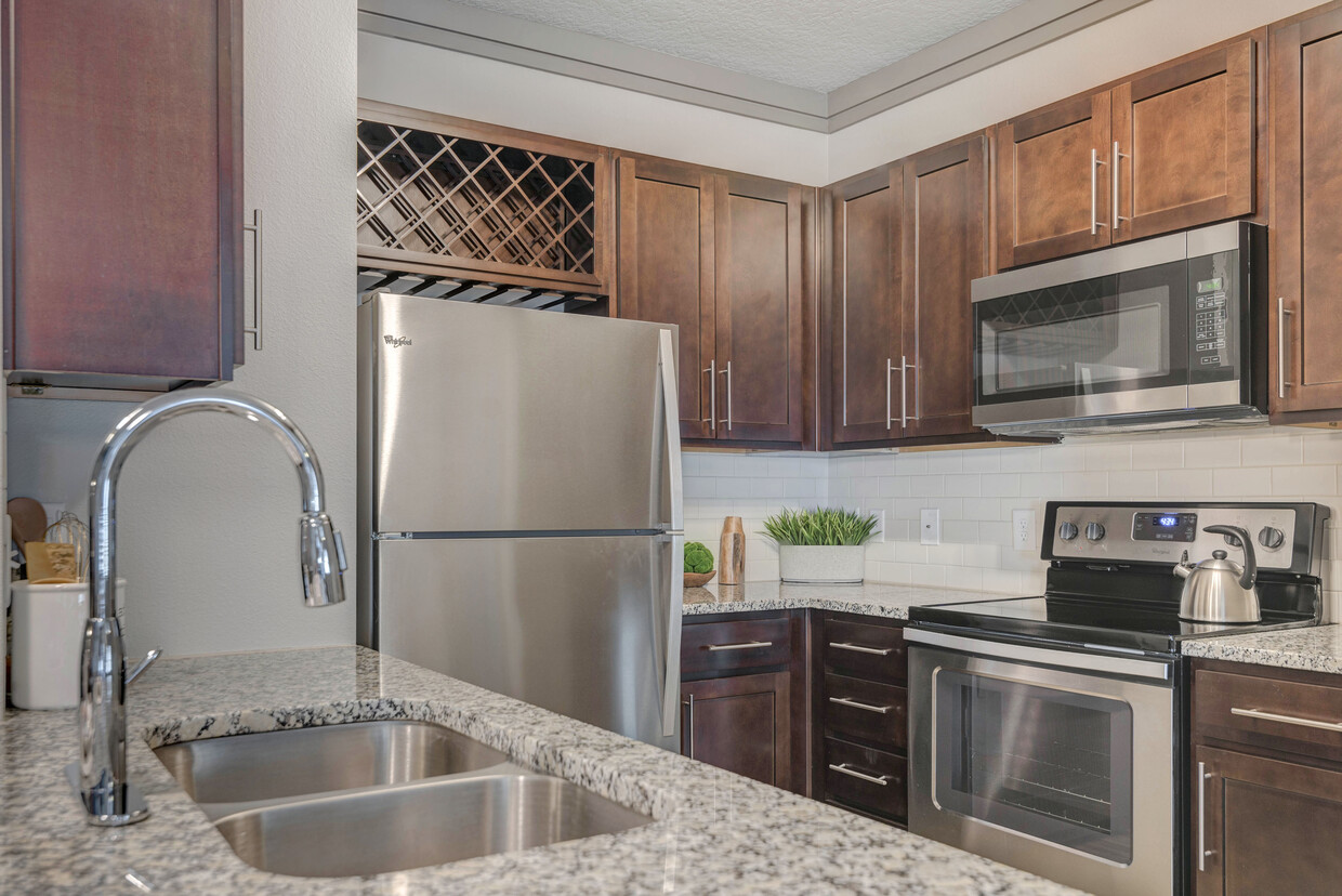 Cocina moderna con gabinetes de madera, salpicadero de azulejos blancos, encimeras de granito y electrodomésticos de acero inoxidable - Avalon Mooresville