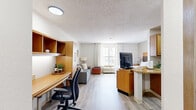 Located at 15155 Katy Fwy in Houston, Texas, this single-floor unit offers a well-organized layout that maximizes every square foot of its compact footprint. The space is designed for functional living, with light wood-tone flooring flowing consistently throughout, creating a cohesive and clean aesthetic across all rooms.

The kitchen is efficiently laid out in a galley style, featuring warm wood cabinetry, granite-look countertops, and black appliances including a range and refrigerator. Ample cabinet storage lines both sides of the kitchen, making practical use of the available space.

The main living area doubles as the bedroom, combining a sleeping space with a seating area. A sofa, flat-screen television, and wooden furnishings share the room alongside the bed, which is flanked by matching wooden nightstands. A window with sheer curtains allows natural light to brighten the space, contributing to an open and airy feel despite the compact size.

The bathroom is clean and modern, with wood-look flooring, a floating-style vanity with an open shelf, and a tub-shower combination featuring marble-style tile surround and a white curtain. The textured ceiling is present throughout the unit, adding a consistent architectural detail to the overall design.