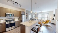 Located at 155 Ames St in Marlborough, MA, this well-appointed 2-bedroom, 2-bathroom residence offers a thoughtfully designed open-concept floor plan. The kitchen is a standout feature, showcasing warm wood-toned cabinetry, a white quartz waterfall island with bar seating, stainless steel appliances, a gas range, and a subway tile backsplash — all illuminated by pendant lighting and track lighting overhead. The kitchen flows seamlessly into the dining area, which benefits from large glass doors that invite natural light and outdoor views, and into the living room, where oversized windows with floor-to-ceiling drapes and a ceiling fan create a bright, comfortable atmosphere. Hardwood flooring runs throughout the main living areas. The primary bedroom is a generous, carpeted retreat with large windows and ample closet space, including a walk-in closet with wire shelving. The second bedroom is equally comfortable, also carpeted and well-lit. Both bathrooms are finished with sleek, wood-grain vanities, wide mirrors with illuminated bar lighting, and tile flooring. A hallway connects the living spaces to the private quarters, contributing to an efficient and functional layout throughout this inviting Marlborough residence.