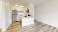 Located at 10237 Western Ave in Downey, CA, this 2-bedroom, 1-bathroom unit offers a clean, modern aesthetic throughout its single-floor layout. Light wood-style flooring flows seamlessly across every room, creating a cohesive and contemporary feel.

The kitchen is a standout feature, showcasing white shaker-style cabinetry, a peninsula with a countertop overhang ideal for casual seating, and a full suite of stainless steel appliances including a refrigerator, gas range, and microwave. A textured ceiling adds subtle character to the open living and kitchen area.

The primary bedroom is a comfortable, well-proportioned room featuring a sliding window with views of the surrounding neighborhood's lush palm trees and greenery, allowing for ample natural light. The second bedroom is equally bright, with a window fitted with vertical blinds and the same light flooring, providing a clean and versatile space.

The bathroom maintains the home's crisp, clean design with white walls, wood-style flooring, a white vanity with a dark-finished faucet, and a mirrored medicine cabinet. A hallway connects the rooms, contributing to an efficient and intuitive layout. Overall, the unit presents a refreshed, move-in-ready interior with a bright and airy ambiance throughout.
