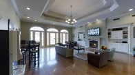 The clubroom at 80 Jefferson Blvd in Fishkill, NY is a thoughtfully designed communal space that combines classic architectural elegance with comfortable, functional living. The room's most striking feature is its tray ceiling, adorned with crown molding and centered by a traditional chandelier, adding a sense of height and grandeur to the space. Recessed lighting throughout ensures the room is well-lit at all times.

A row of arched French doors lines one wall, allowing an abundance of natural light to flood the interior while providing views of the outdoors. The rich hardwood flooring extends throughout, grounding the space with warmth and character.

On the opposite wall, a classic white fireplace serves as a focal point, flanked by built-in shelving and cabinetry that offer both display and storage options. A wall-mounted flat-screen television above the fireplace makes this an ideal gathering space for entertainment.

The layout accommodates multiple seating arrangements, including a plush sofa and lounge chairs grouped around a coffee table, as well as a casual dining area with bar-height seating. The soft, neutral color palette of sage green walls and white trim creates a refined yet inviting atmosphere, making this clubroom a versatile and welcoming retreat for residents and guests alike.