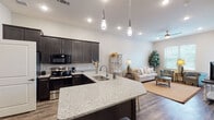 This thoughtfully designed 1-bedroom, 1-bathroom residence offers a comfortable and functional single-floor layout. The open-concept kitchen and living area serves as the heart of the home, featuring dark espresso shaker-style cabinetry, granite countertops, stainless steel appliances — including an electric range and dishwasher — and a peninsula with an undermount sink and pendant lighting overhead. Wood-look flooring flows throughout the main living areas, anchoring the bright, neutral color palette that gives the space an airy, welcoming feel.

The living area is generously sized, accommodating a full seating arrangement and benefiting from natural light through large windows. The bedroom is a peaceful retreat with plush carpeting, windows with outdoor views, and room for substantial furniture. The full bathroom is well-appointed with dark cabinetry, granite vanity countertop, tile flooring, a linen tower for added storage, and direct access to a walk-in closet. Recessed lighting and ceiling fans are featured throughout, contributing to both functionality and comfort. Overall, the unit presents a clean, modern aesthetic with quality finishes in a practical, efficiently organized floor plan.