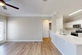Located at 2020 Business Center Dr in Pearland, TX, this thoughtfully designed one-bedroom, one-bathroom residence offers a clean, modern aesthetic throughout its single-floor layout. Light wood-style flooring flows seamlessly across every room, complemented by neutral gray and white tones that create a bright, cohesive atmosphere. Crown molding adds an elegant finishing touch to the living areas and bedroom.

The open-concept living, dining, and kitchen area forms the heart of the home. The kitchen features white shaker-style cabinetry, white quartz countertops, a stainless steel undermount sink, and stainless steel appliances, including a range and dishwasher. A peninsula counter provides additional workspace and casual dining potential. Natural light enters the living room through windows flanking a private entry door, while a ceiling fan overhead ensures year-round comfort.

The bedroom is a comfortable retreat, finished with crown molding and its own ceiling fan. It accesses a walk-in closet with built-in shelving, offering ample storage. The full bathroom includes a white vanity with quartz countertop, a tiled shower-tub combination, and clean, neutral finishes throughout.

A dedicated in-unit laundry area accommodates a full-size washer and dryer, adding everyday convenience. The hallway connects all spaces efficiently, completing this well-organized and move-in-ready home.